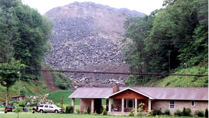 A home and car in the driveway. Behind them, is the result of mountaintop removal, which looks like a pile of dark rubble.