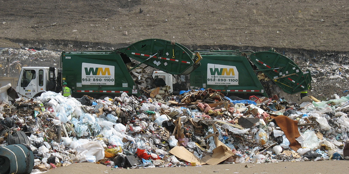 Photo shows two garbage trucks dumping their contents into a landfill.