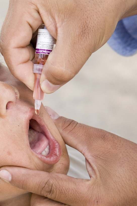 La photo montre un enfant recevant un vaccin oral à l'aide d'un compte-gouttes.