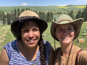 Melanie Kirby y Ang Roell, apicultora radicada en Nueva México, sonríen a la cámara en un campo con colmenas de fondo