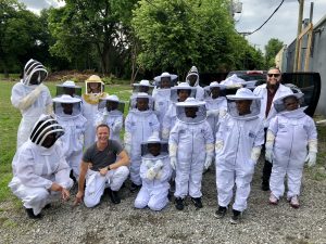 Brian Peterson-Roest se arrodilla y sonríe entre un grupo de jóvenes estudiantes en trajes completos de abeja en un campo