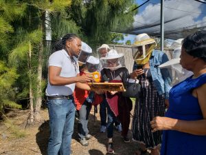 Alwyn Simeina con marco de abeja en mano educando a grupo comunitario afuera