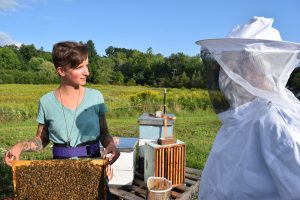 Ang Roell sosteniendo el marco de la colmena y mirando a alguien en traje completo de abeja
