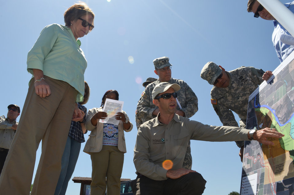 Un hombre señala un mapa que detalla la restauración del hábitat, rodeado por un grupo de personas, entre ellas dos con uniforme del Ejército.