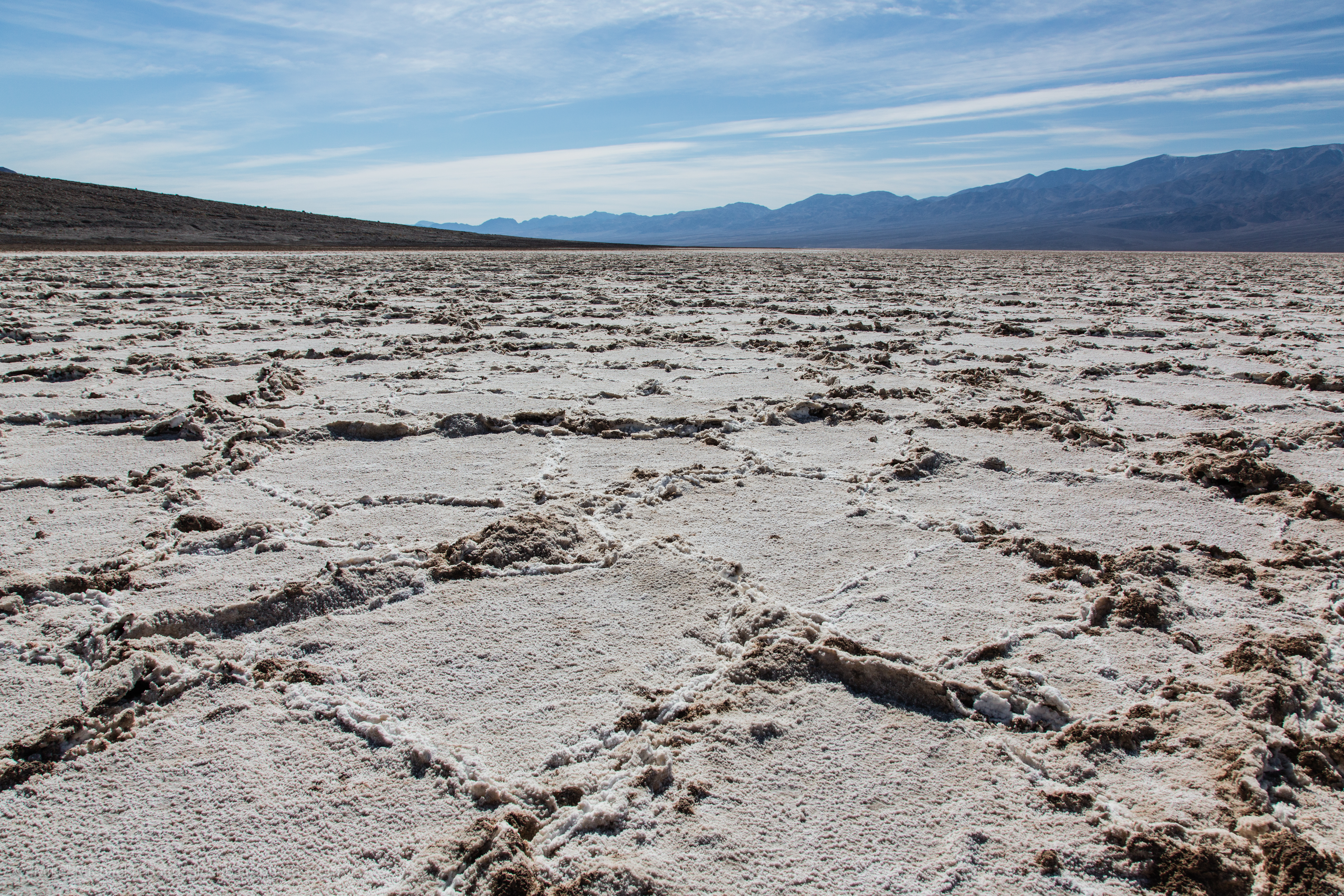 Flat landscape with hexagonal salt formations. Mountains are in the background, but the salt flats appear devoid of multicellular life.