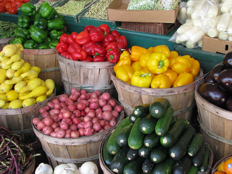 Baskets of bell peppers, eggplants, squashes, potatoes, and zucchinis at a farmers' market 