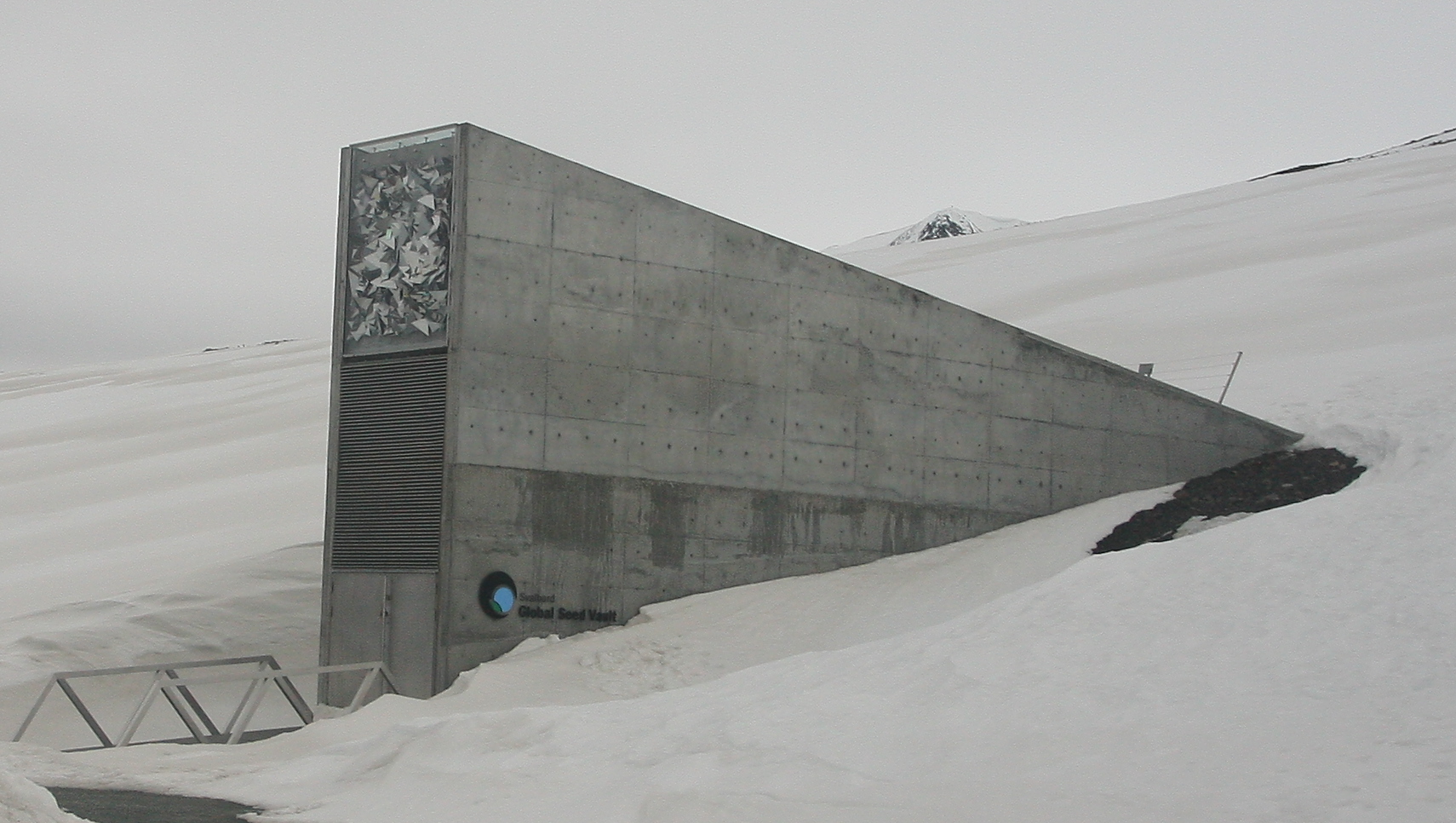 A narrow rectangular building is partially buried in a snowy hillside, keeping the seeds inside the vault cool.