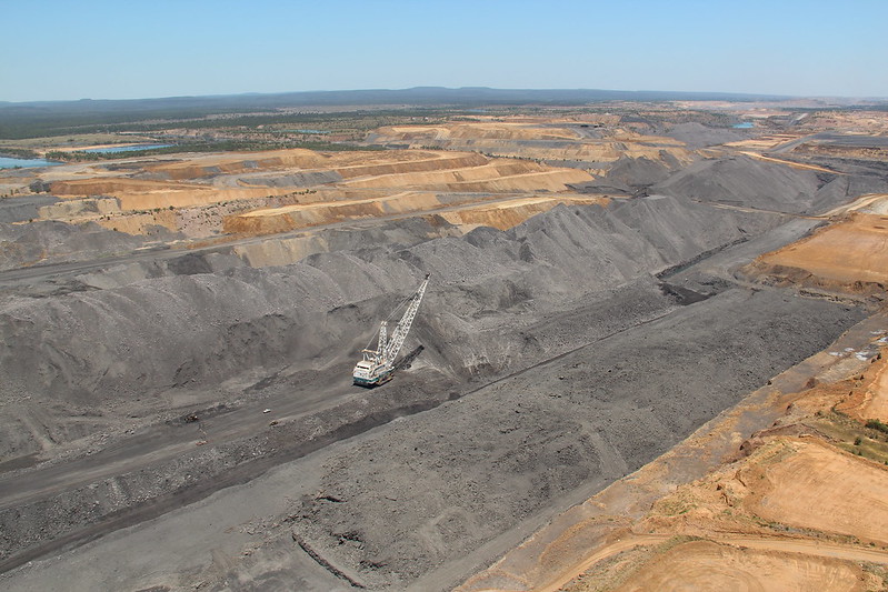 A coal mine with heavy machinery collecting the dark coal. Bare, displaced soil surrounds the coal deposit.