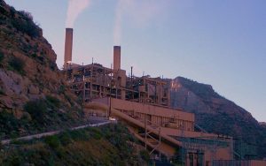 Smoke released from a brown, metal coal power plant on a hill