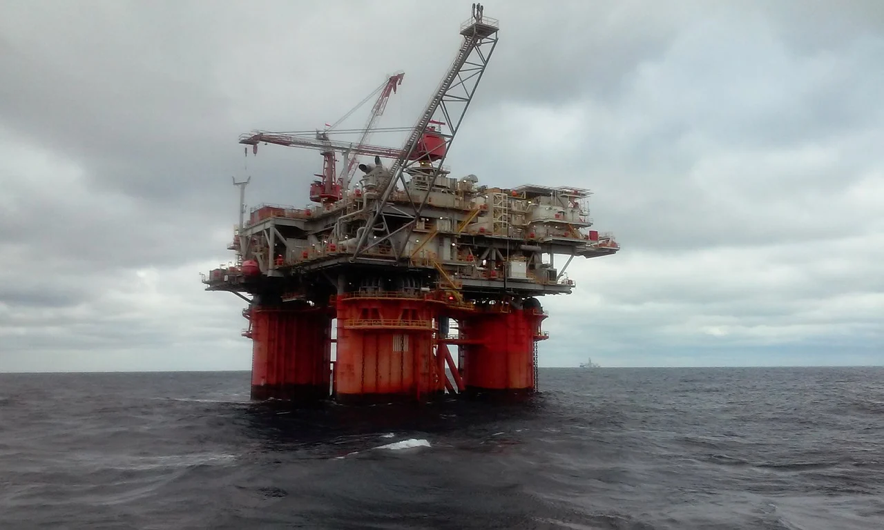 Four red pillars support a platform that emerges from the ocean, supporting offshore drilling