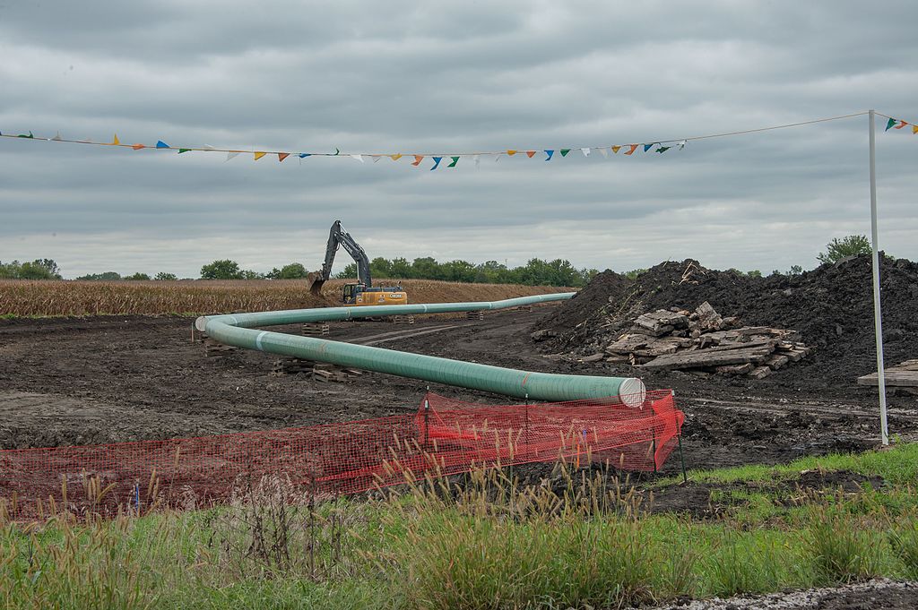 Soil is displaced, and a thick, pale blue tube (the Dakota Access Pipeline) is assembled.