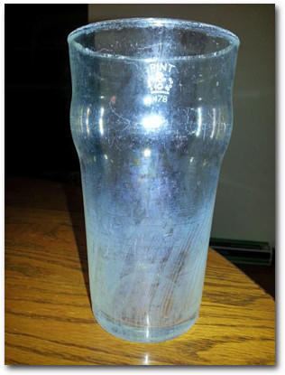 A glass clouded with residue from hard water sits on a wooden table.