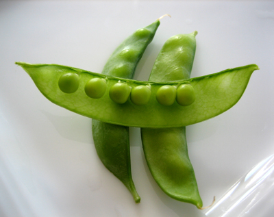 A group of peas, two in their green pods, one group of peas are outside on the pod