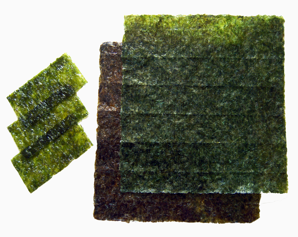Nori, roasted sheets of seaweed used in Japanese cuisine for sushi. Smaller pieces are also pictured, already seasoned with sesame oil and spices.