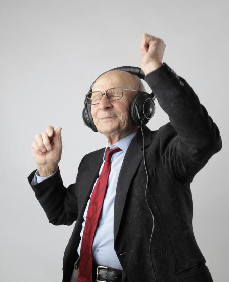 A photo of an old man wearing glasses and a suit with headphones while dancing.