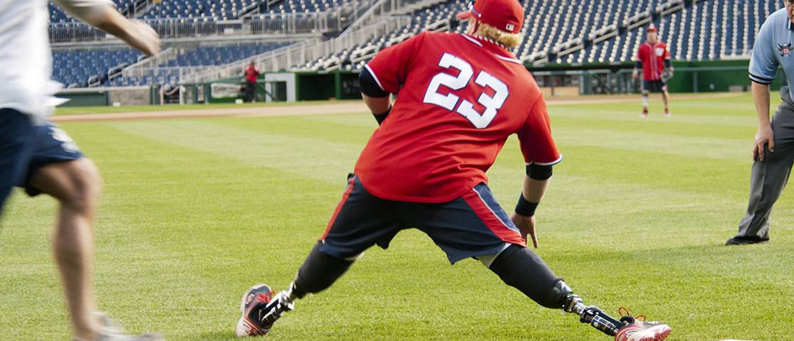 Photo shows a man with prosthetic legs stretching out while playing baseball.