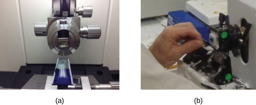 Photograph a shows a blue solid specimen sits below a mechanical dial. Photograph b shows a person holding a dial on a machine.