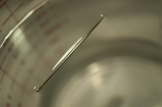 A needle floats in a glass of water.
