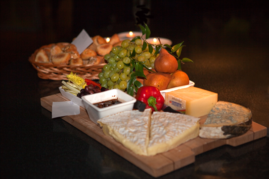 A foto mostra uma variedade de queijos, frutas e pães servidos em uma bandeja.