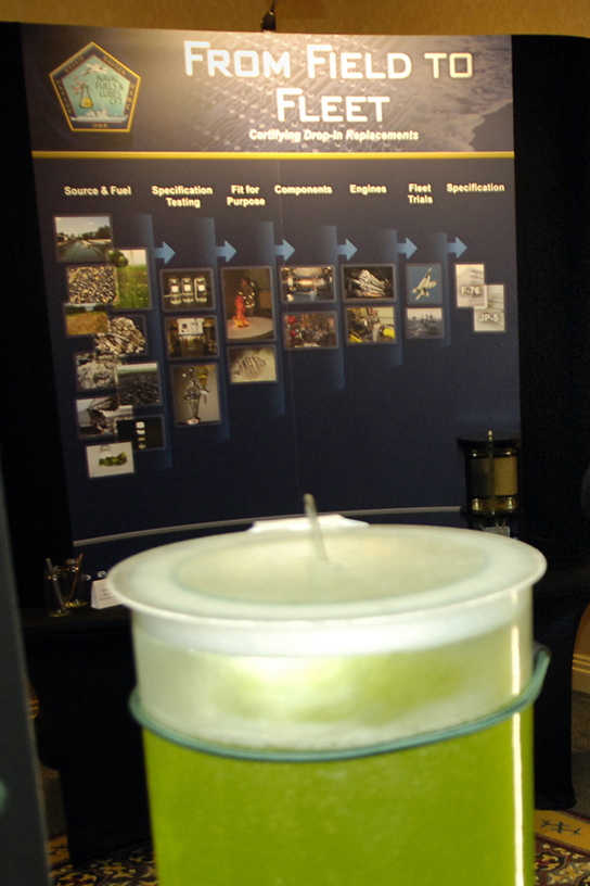 Una foto de un contenedor grande de líquido verde, con una exhibición en el fondo con el título “De Campo a Flota”.