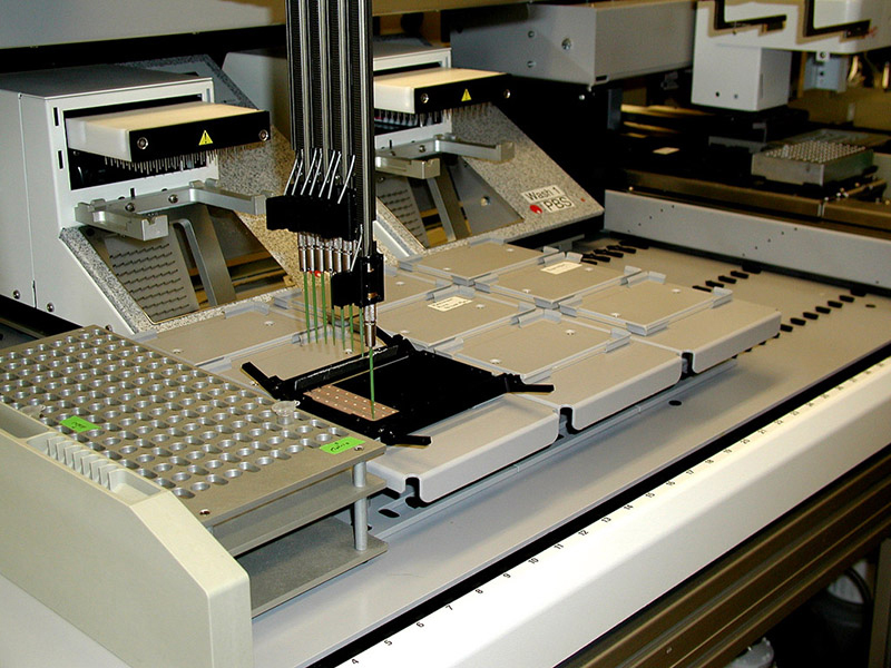 La foto muestra un analizador de patrones de proteínas. Se trata de una gran pieza de equipo sobre una mesa con pipetas al final de tubos largos de acero.
