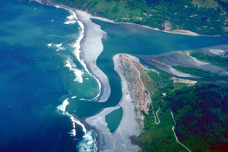 Esta foto muestra una vista aérea del océano a la izquierda, y un río a la derecha desembocando en el océano.